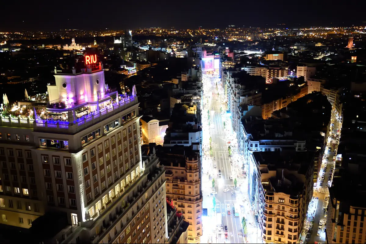 Gran Vía v noci z ptačí perspektivy, rozsvícené výlohy a provoz mezi vysokými budovami.