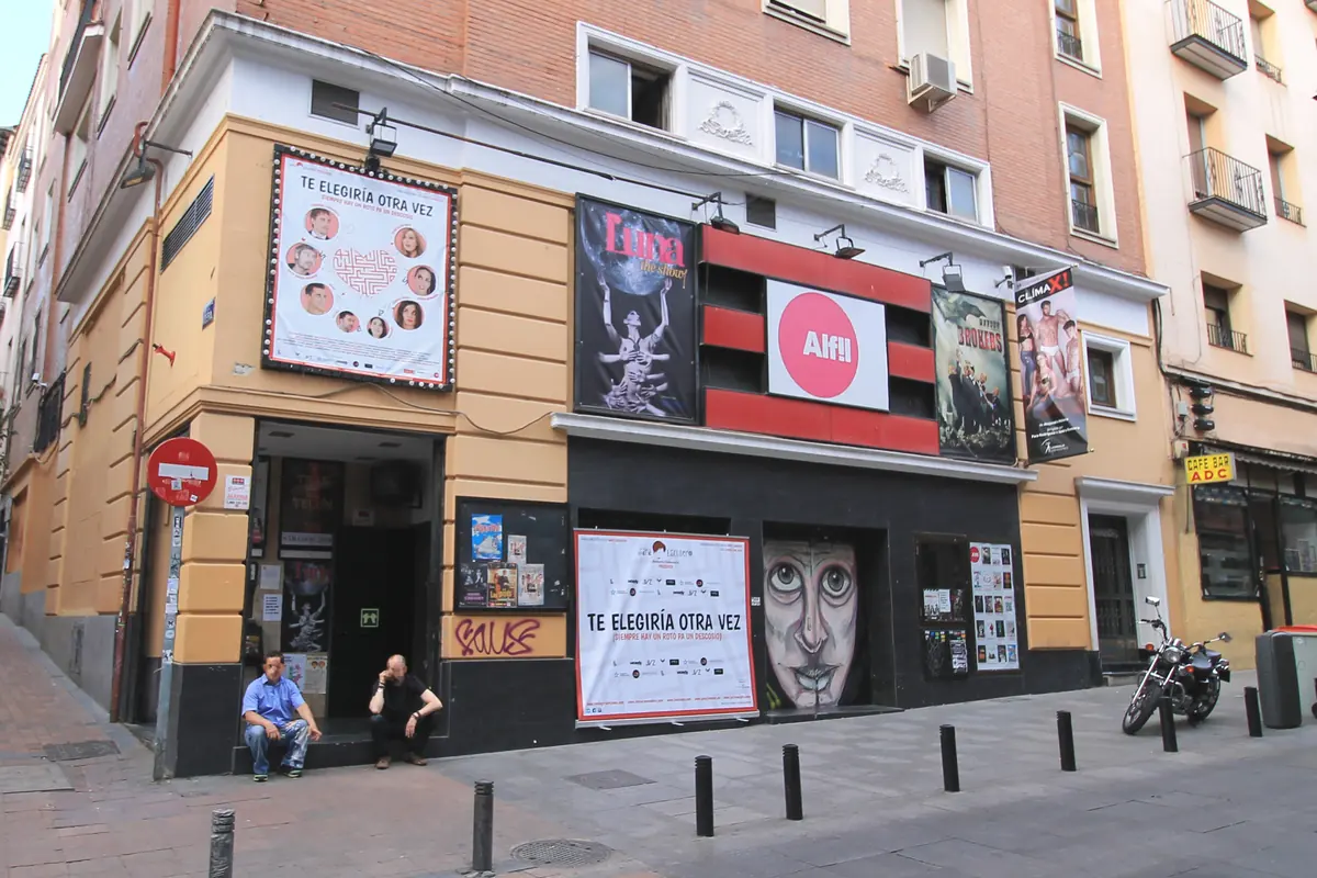 Ulice před divadlem Teatro Alfil na rohu v Malasañi, s plakáty, červenobílým nápisem a motorkou zaparkovanou u obrubníku.